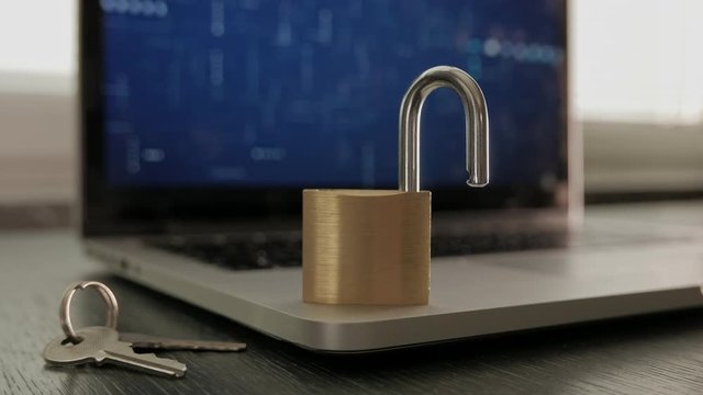 Unlocked padlock on top of a laptop computer, with keys next to it.