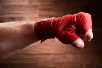 Close up image of fist of a boxer with red bandage against brown background.