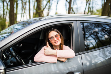 Woman sitting in the car and showing thumbs up in the street