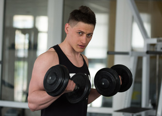 Fototapeta na wymiar Strong muscular male sportsman working out in gym with big dumbbells. A fitness instructor doing exercises. Fitness club gym training lifestyle commercial concept.