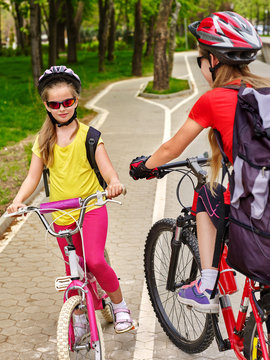 Bicycle path and sign with children. Girls wearing helmet with rucksack ciclyng ride. Kids are on white bike lane. Alternative to urban transport. Oncoming traffic. People support healthy lifestyle.