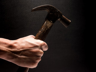 Male hand holding hammer on black background.