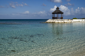 Clear warm water, blue sky, and a beach-side gazebo in the Caribbean