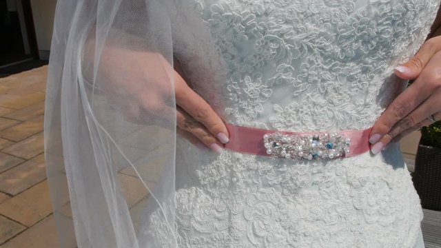 bride adjusts the pink belt on a white wedding dress