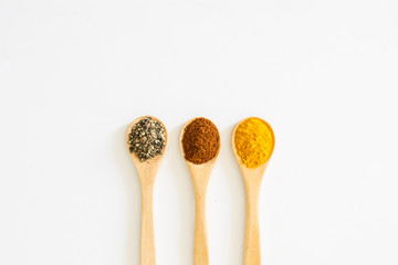 Turmeric, Paprika and Black Pepper in wooden spoon over white background.