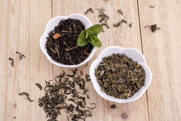 Green and black tea leaves in ceramic bowl on wood background