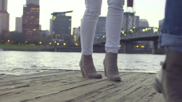 Closeup Of Young Women's Feet/Legs As They Dance Around End Of Dock, Cityscape Behind Them