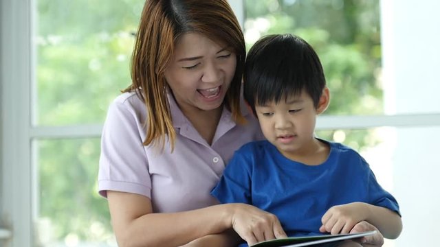 Asian mother and her son reading a book together,slow motion