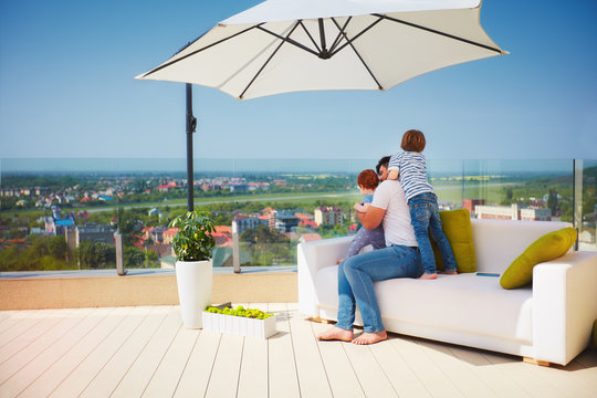happy family enjoying the view, relaxing on couch at roof top terrace at warm sunny day