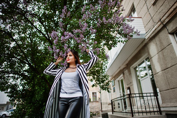 Fototapeta premium Fashionable woman look with black and white striped suit jacket, posing against lilac tree. Concept of fashion girl.