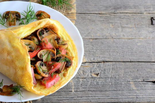 Mushrooms and tomatoes omelette. Homemade omelette stuffed with mushrooms, tomatoes and dill on a plate and vintage wooden background with copy space for text. Easy vegetarian breakfast. Rustic style