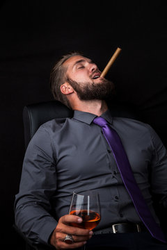 Portrait eines jungen relaxenden Geschäftsmannes mit Getränk und Zigarre