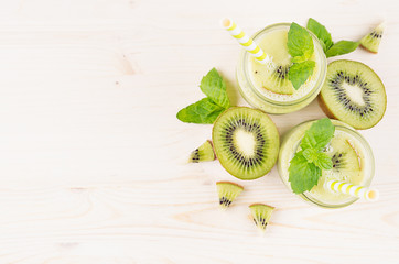 Fototapeta na wymiar Decorative frame of green kiwi fruit smoothie in glass jars with straw, mint leaf, cute ripe berry, top view. White wooden board background, copy space.