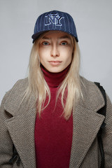 Portrait of a blonde girl in wool coat and baseball hat with no make up.