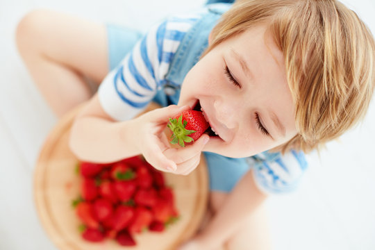 cute happy kid eating tasty ripe strawberries