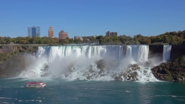 View of tour boat cruising at the base of misty Niagara Falls as seen from the Skylon Tower. Whitewater waterfalls American & Bridal Veil Falls, touristic hotels and New York skyline in the background