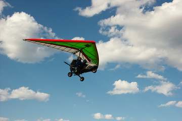 The motorized hang glider flying on background blue sky with clouds.