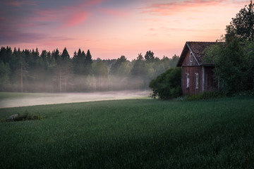 Scenic landscape with field and old cottage at summer night in Finland