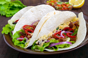 Tacos is a traditional Mexican dish. Tortilla stuffed with chicken, bell and hot peppers, beans, lettuce, cheese, blue onion with salsa sauce on dark wooden background. Close up