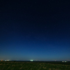 Fototapeta na wymiar Stars in the night sky with city lights on the horizon. The landscape is photographed by moonlight.