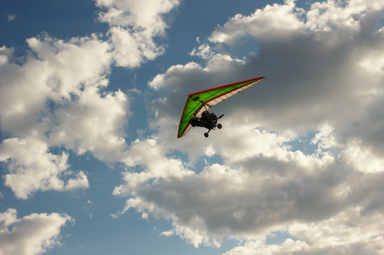 The motorized hang glider flying on background blue sky with clouds.
