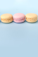 Three sweet colorful macaroons on blue table background.