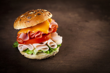 Delicious sandwich with ham, lettuce, tomato, chicken and cheddar cheese on a wooden table