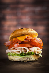 Delicious sandwich with ham, lettuce, tomato, chicken and cheddar cheese on a wooden table