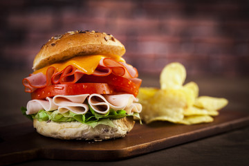 Delicious sandwich with ham, lettuce, tomato, chicken and cheddar cheese on a wooden table
