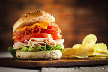 Delicious sandwich with ham, lettuce, tomato, chicken and cheddar cheese on a wooden table
