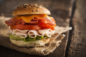 Delicious sandwich with ham, lettuce, tomato, chicken and cheddar cheese on a wooden table