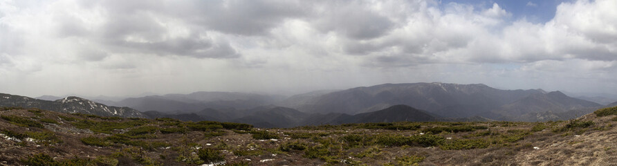 Fototapeta premium Panoramic landscape with peaks of mountains, hills, forest and sky with contrasting clouds