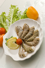 Jumbo headless shrimps with lemon and cherry tomato on white plate