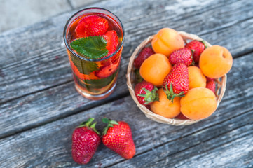 Wicker basket with strawberries and apricots, top view, glass with detox drink and mint leaves, natural wood background