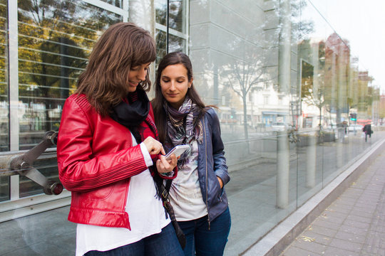 Women using smartphone while standing  against glass wall