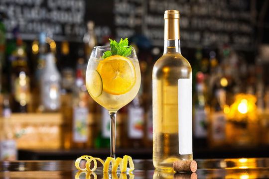 Glass of sangria and white wine bottle at bright bar counter background.