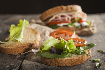 Tasty sandwich with ham, cheese, tomato and lettuce on wooden background