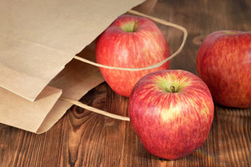 Apples on wooden background. Apples roll out of a paper bag.