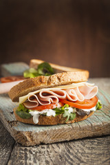 Smakelijke sandwich met ham, kaas, tomaat en sla op houten achtergrond