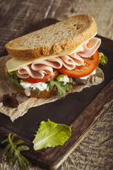 Tasty sandwich with ham, cheese, tomato and lettuce on wooden background