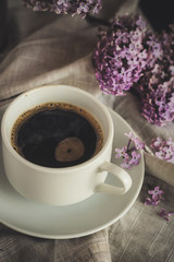 A portion of coffee in a white cup on the table, a bouquet of lilac