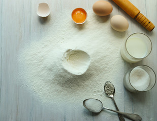 Eggs, flour, milk, sugar, on a white wooden table.