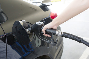Close-up photo of hand holding fuel pump and refilling car at petrol station
