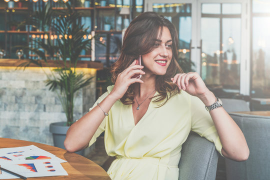 Young attractive businesswoman sitting alone at table in cafe and calling by cell phone.