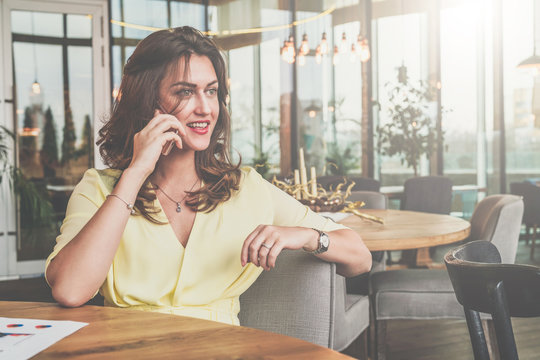 Young attractive businesswoman sitting alone at table in cafe and calling by mobile phone.