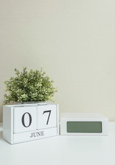 White wooden calendar with black 7 march word with clock and plant on white wood desk and cream wallpaper textured background in selective focus at the calendar