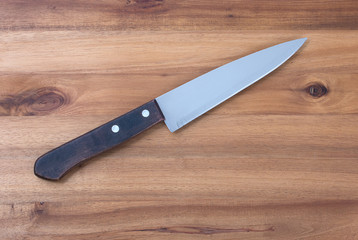 Chef's kitchen knife with wooden handle on a dark cutting board background, top view, close-up.