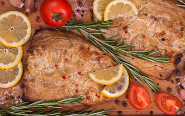 Baked mackerel with slices of lemon, rosemary, tomatoes, garlic, salt, red and black pepper on wooden cutting board. Top view, close up.