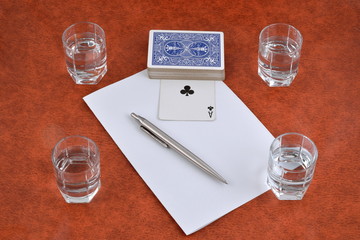 A deck of playing cards, pen, paper and stacks of vodka on the table
