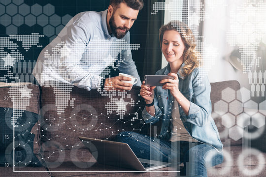 Young woman in denim shirt,sitting at home on couch and using laptop.Nearby stands man and looking on computer screen. - Powered by Adobe